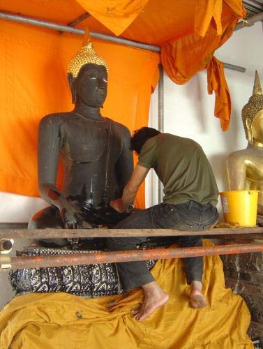 Man repairing gold leaf on a statue of the Buddah