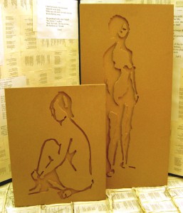 Two wooden blocks with lasered sketches set infront of sewed book pages