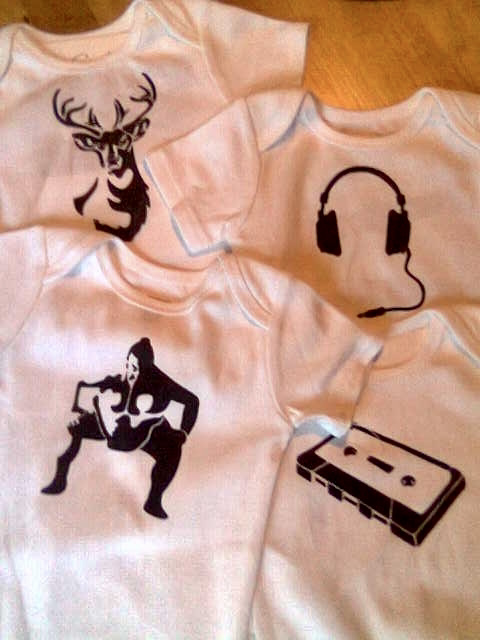 Four baby onesies with stamped designs of a stag, sumo wrestler, headphones, and a cassette tape