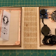 Interior view of bibliocircuitry project with paper circuit on the left and microcontroller with audio connections on the right